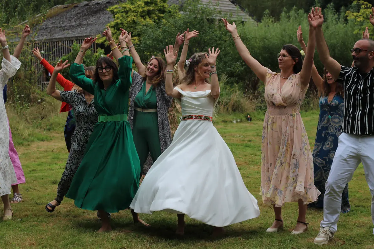 The bride dancing in a ring of guests in the field, everyone with their arms in the air