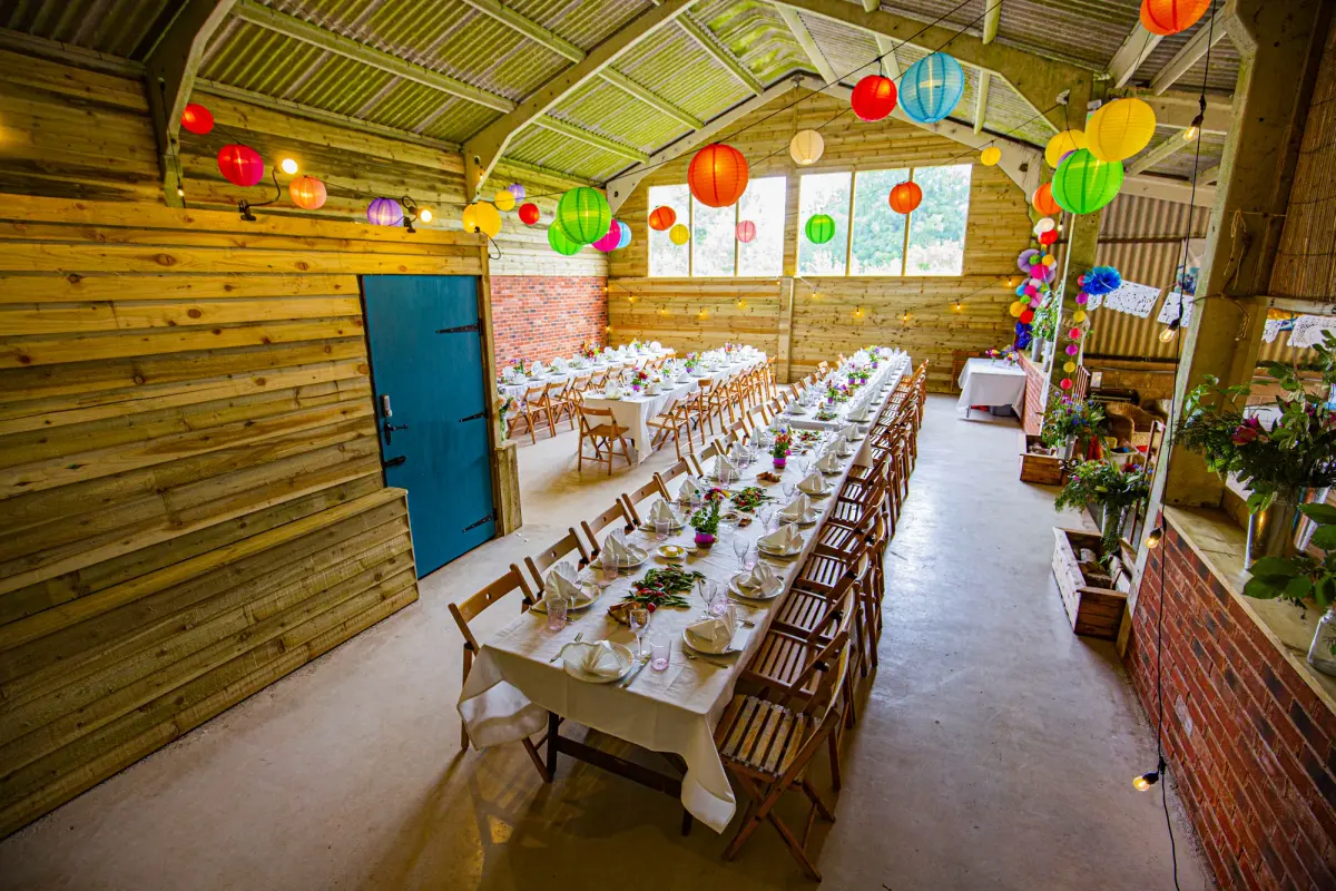 Long tables laid for a wedding breakfast in the barn, hung with paper lanterns