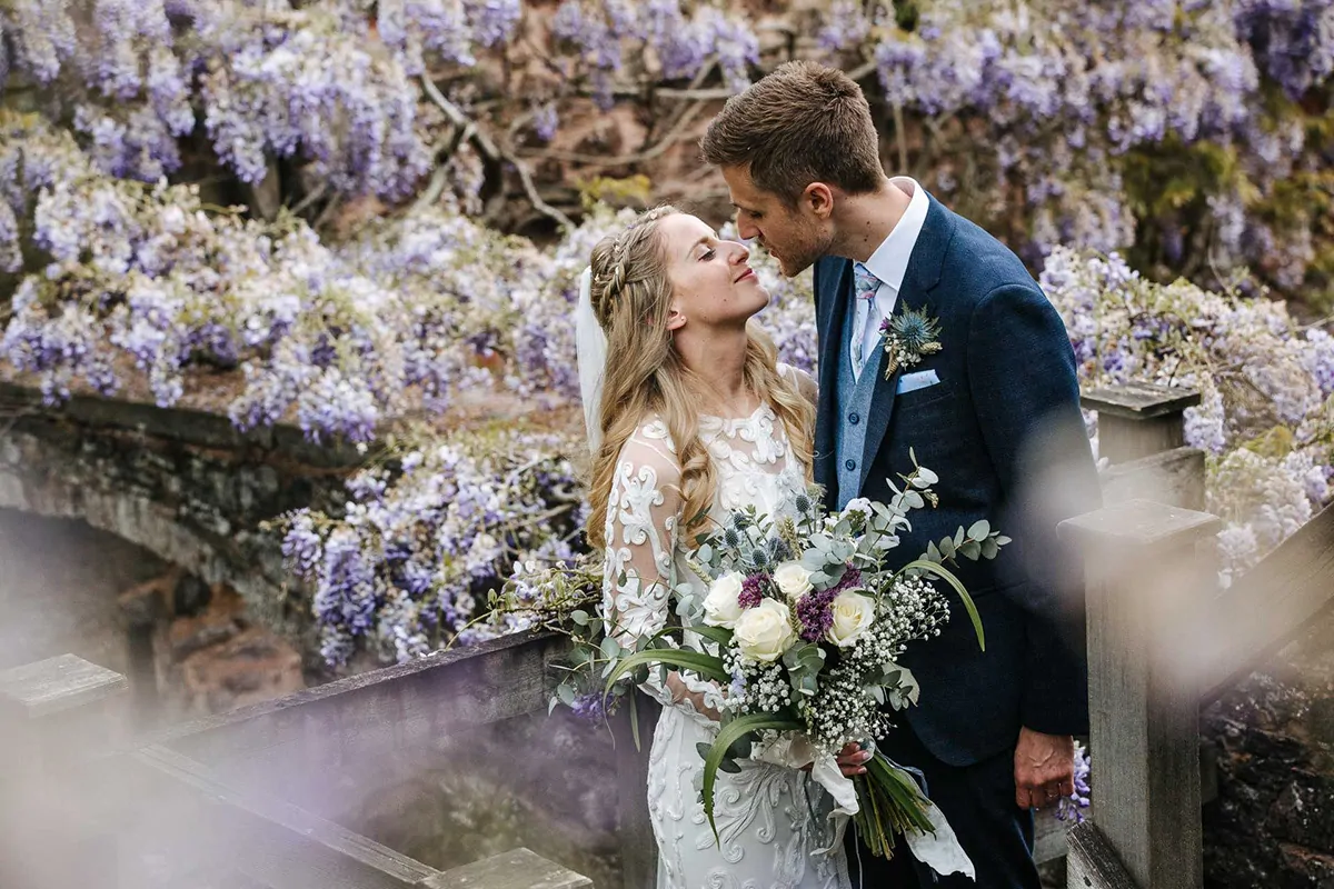 A couple on the bridge beneath the wisteria, the bride holding a white and green bouquet