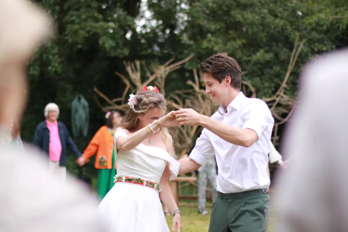 A bride and a guest dancing on the grass, guests looking on