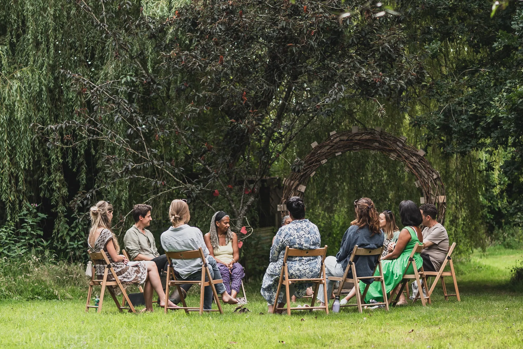 A facilitated circle of people seated on chairs in the trees