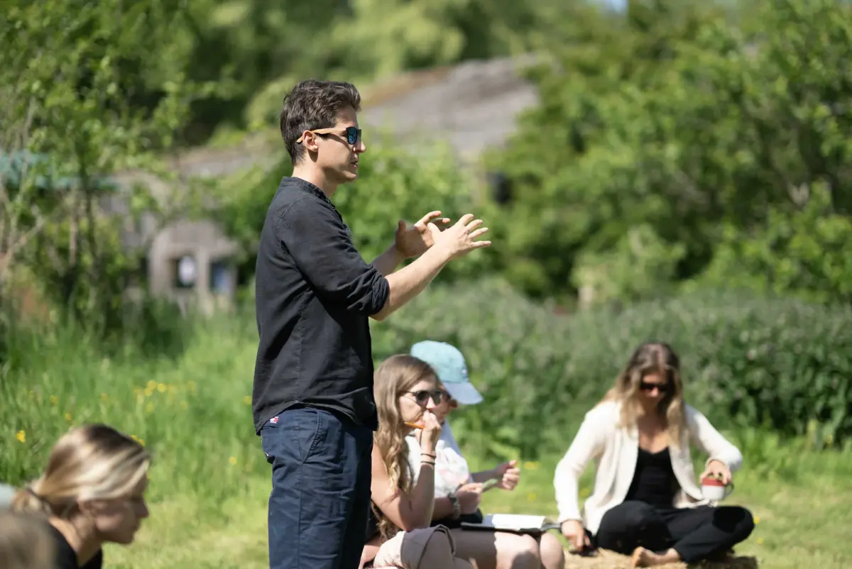 A facilitator speaking to a group seated outdoors among the trees