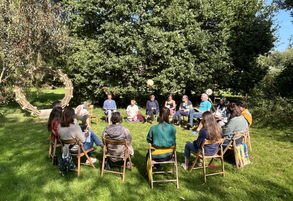 A facilitated circle of people on the lawn beside the woven portal sculpture