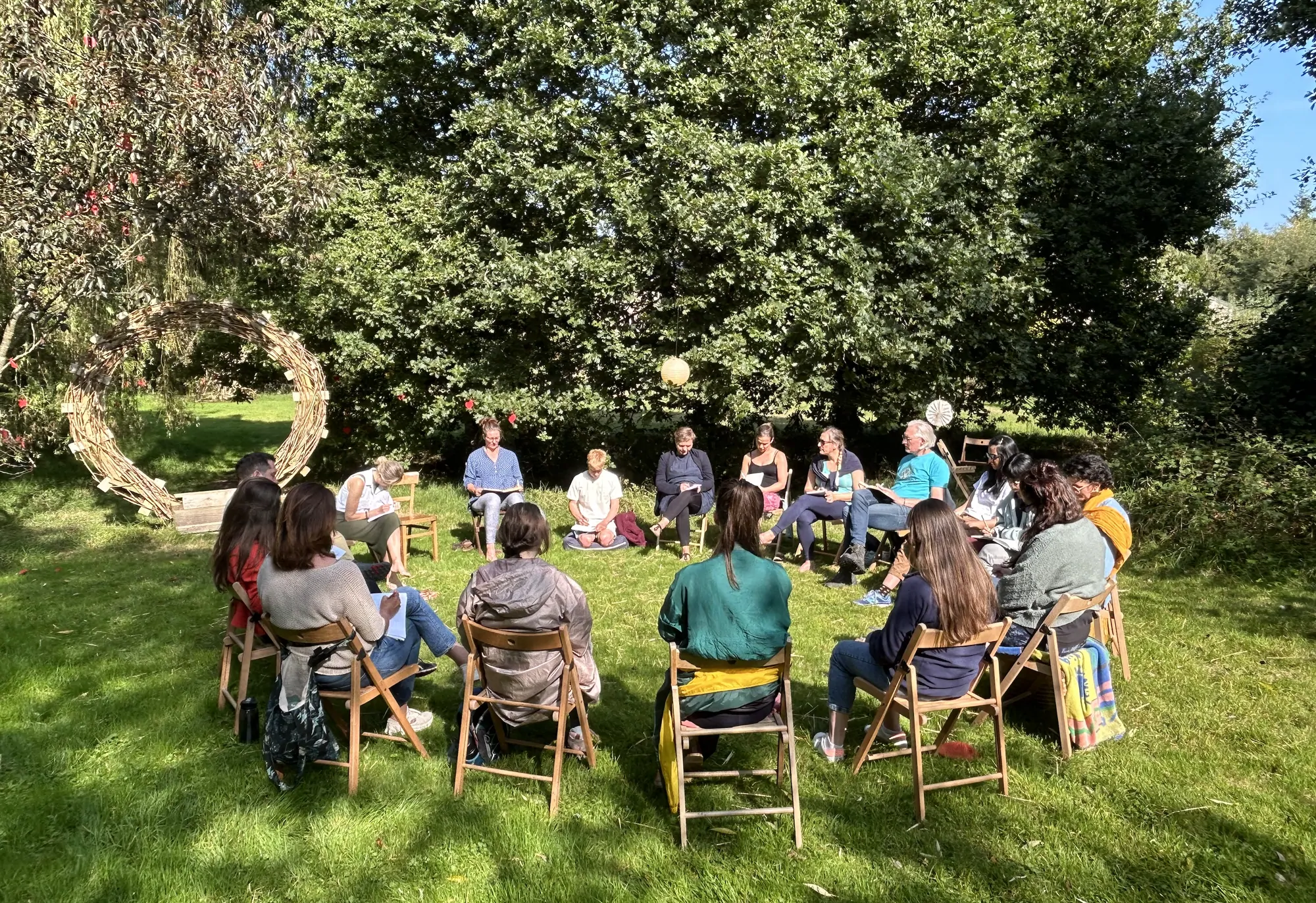 A facilitated circle of people on the lawn beside the woven portal sculpture